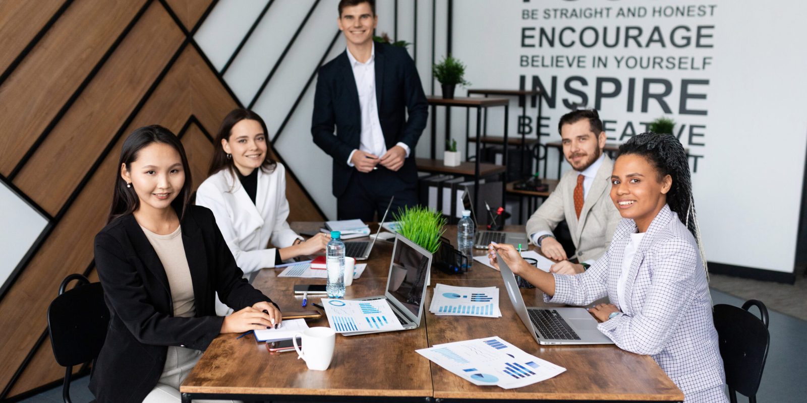 colleagues in the office at a large working table look at the camera.